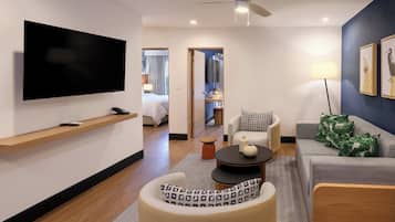 Et moderne hotelværelse med et fladskærms-tv, en sofa, en lænestol, et lille bord og en loftsvifte.