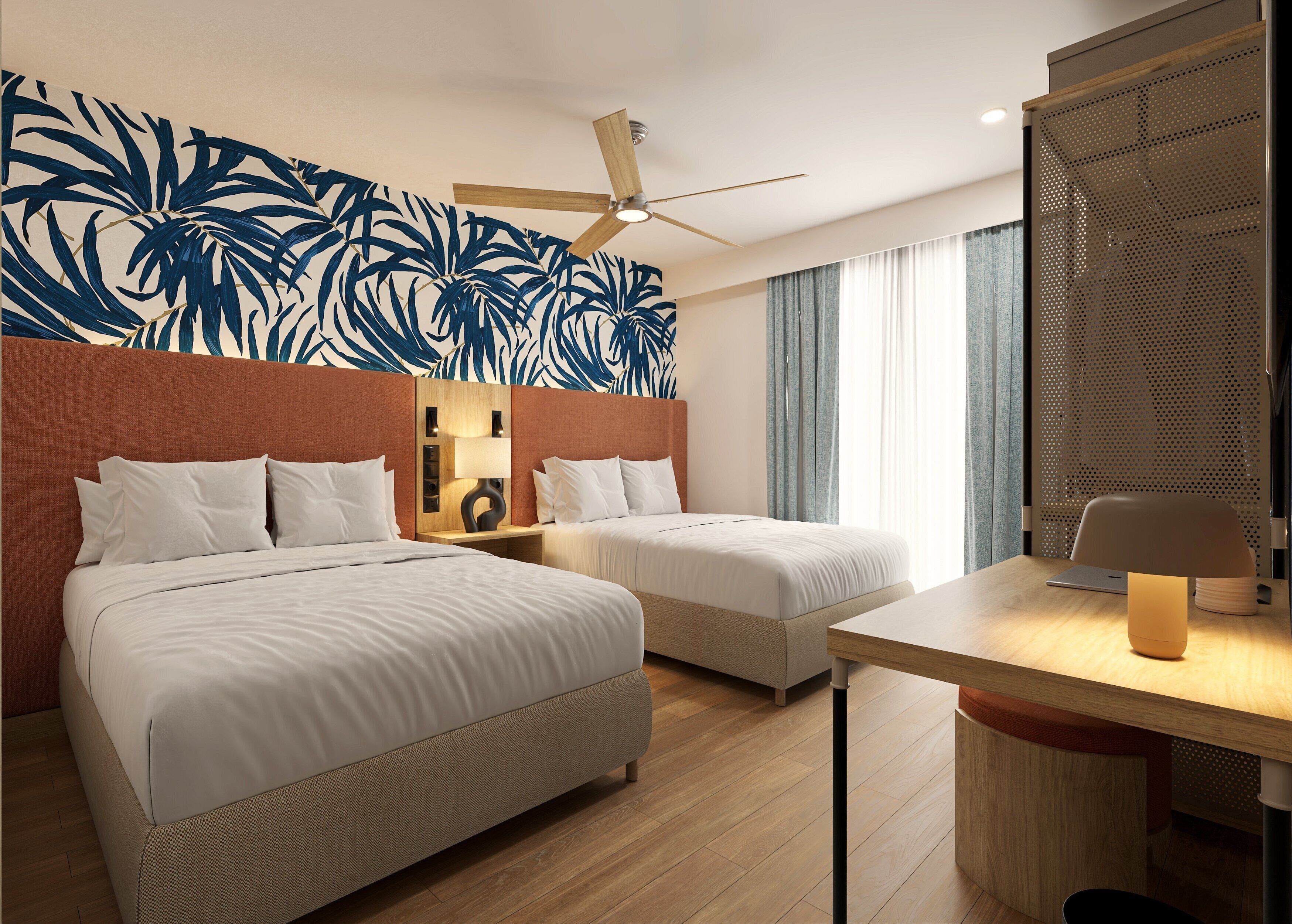 A hotel room with two beds, a ceiling fan, a desk with a lamp, and a large window with curtains.