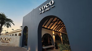 A modern building with a sign reading 'VOCO BY IHG' and a large potted plant. - voco Surfside Aruba by IHG (Oranjestad)
