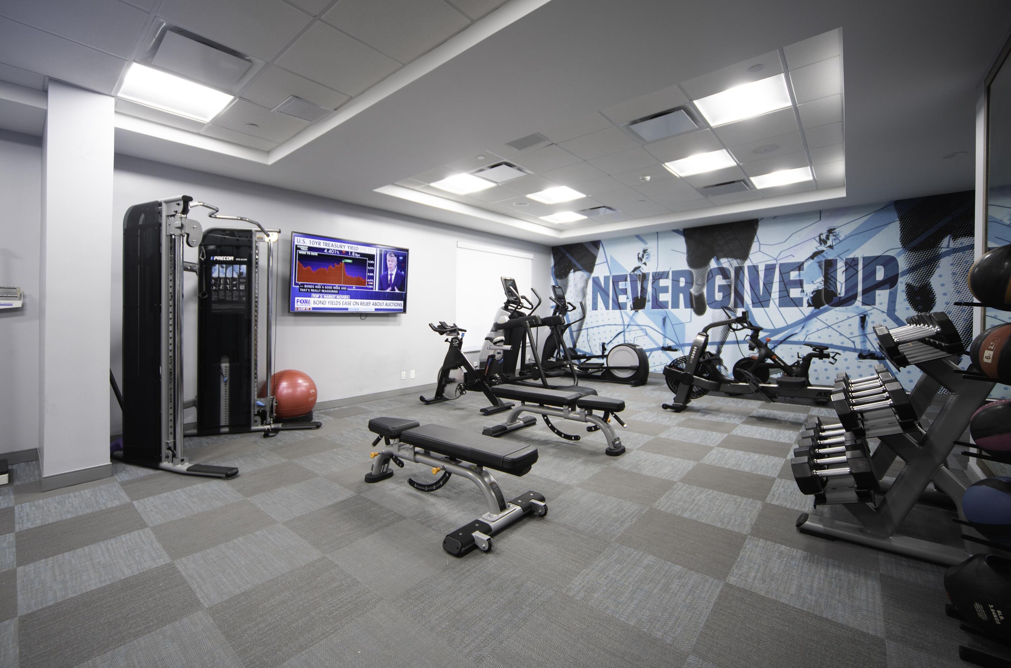 Un gimnasio con diversos equipos de ejercicio, una pared motivacional y un televisor que muestra un gráfico.