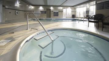 Piscina interior con normas y señales de seguridad claras, una silla de salvavidas y un área de descanso con sillas.
