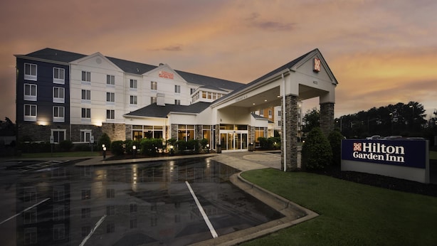 A Hilton Garden Inn with a covered entrance, stone pillars, and a parking lot at dusk.