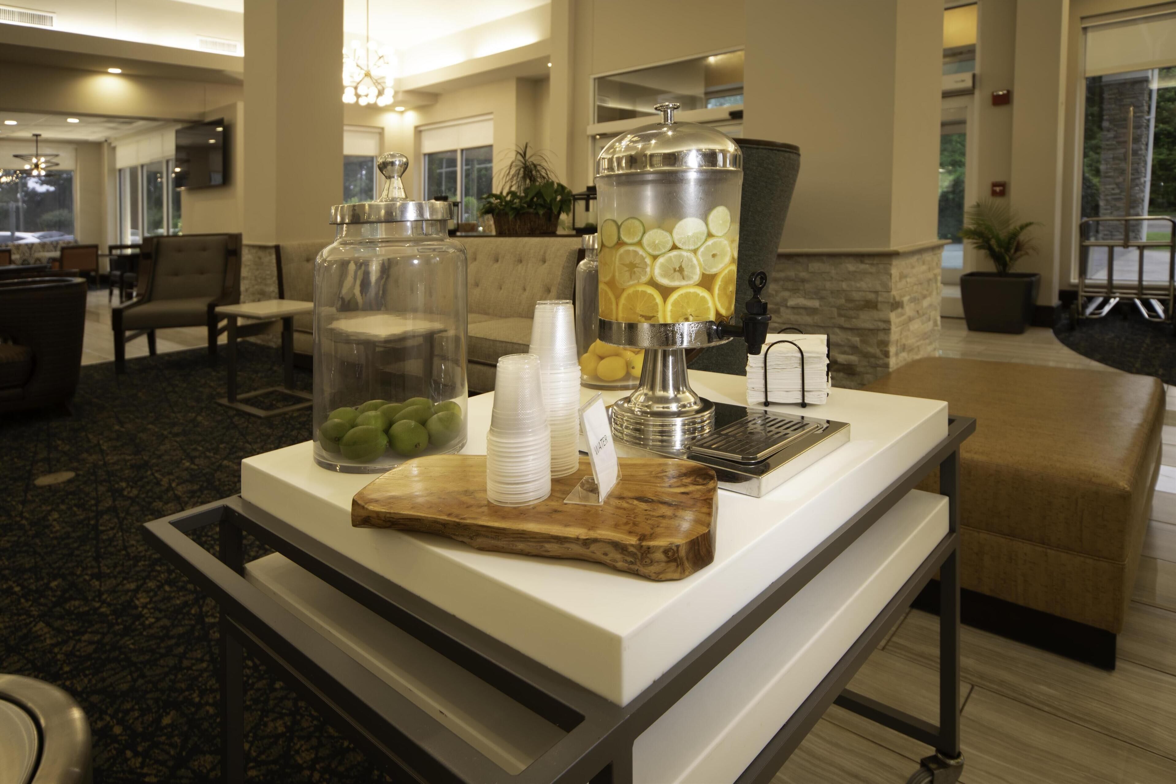 A buffet setup with a punch bowl, a glass container with fruits, and a wooden board.