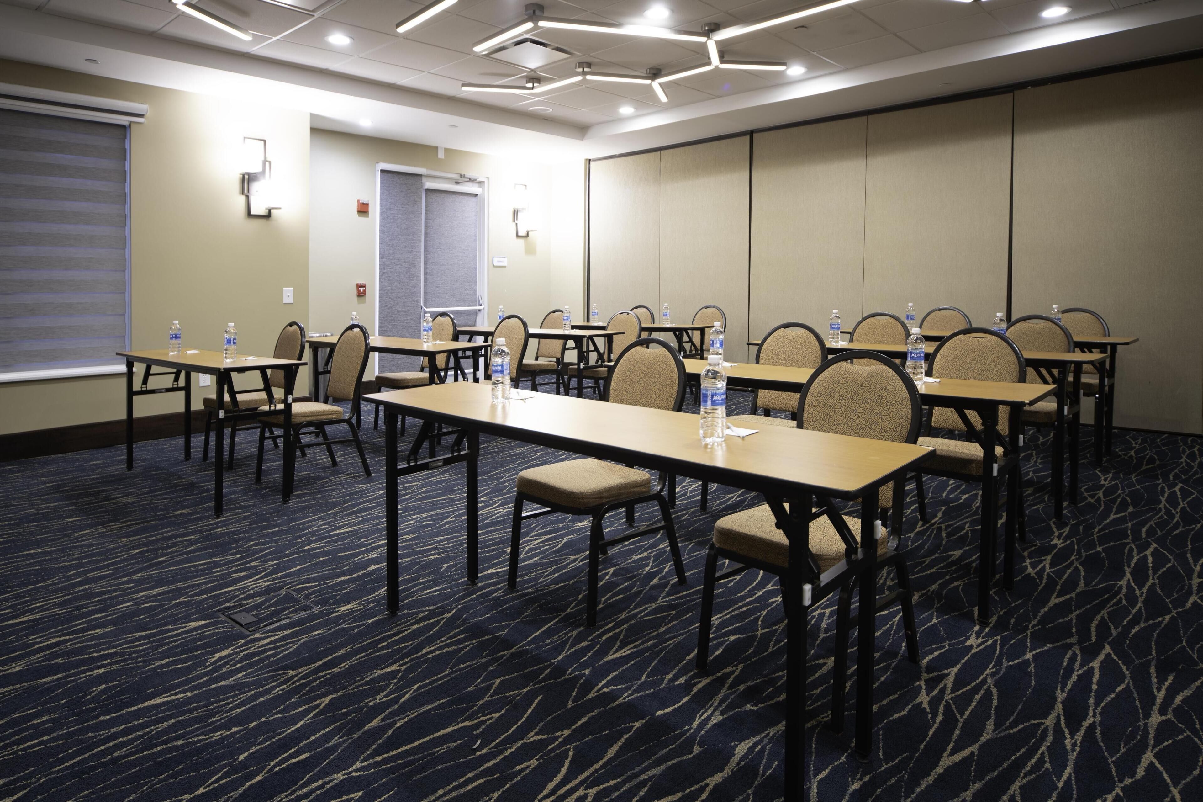 A conference room with tables and chairs, water bottles on each table, and a carpeted floor.