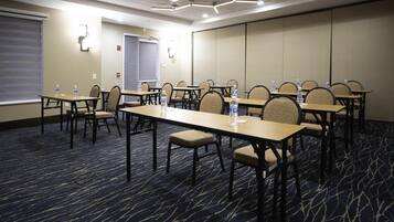 A conference room with tables and chairs, water bottles on each table, and a carpeted floor.