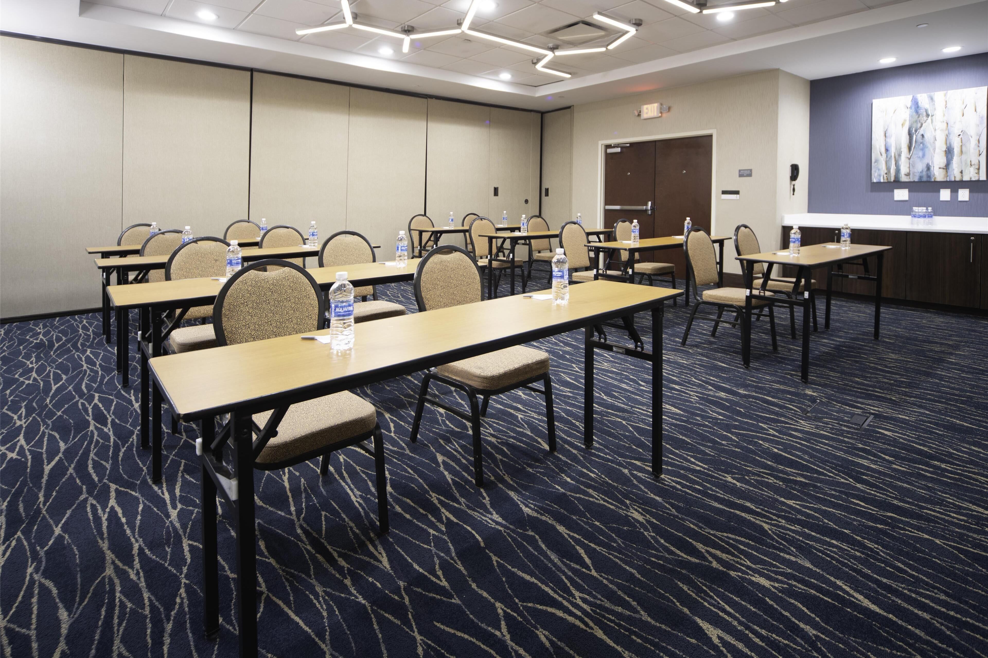 Un salón de conferencias con mesas, sillas y botellas de agua.