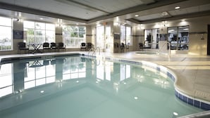 A large indoor swimming pool with clear water, surrounded by windows and chairs.