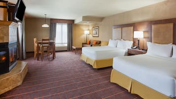 Habitación de hotel con dos camas, televisión, chimenea, zona de comedor y ventana con cortinas.
