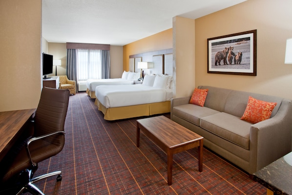 A hotel room with two beds, a sofa, a desk, a chair, and a television.
