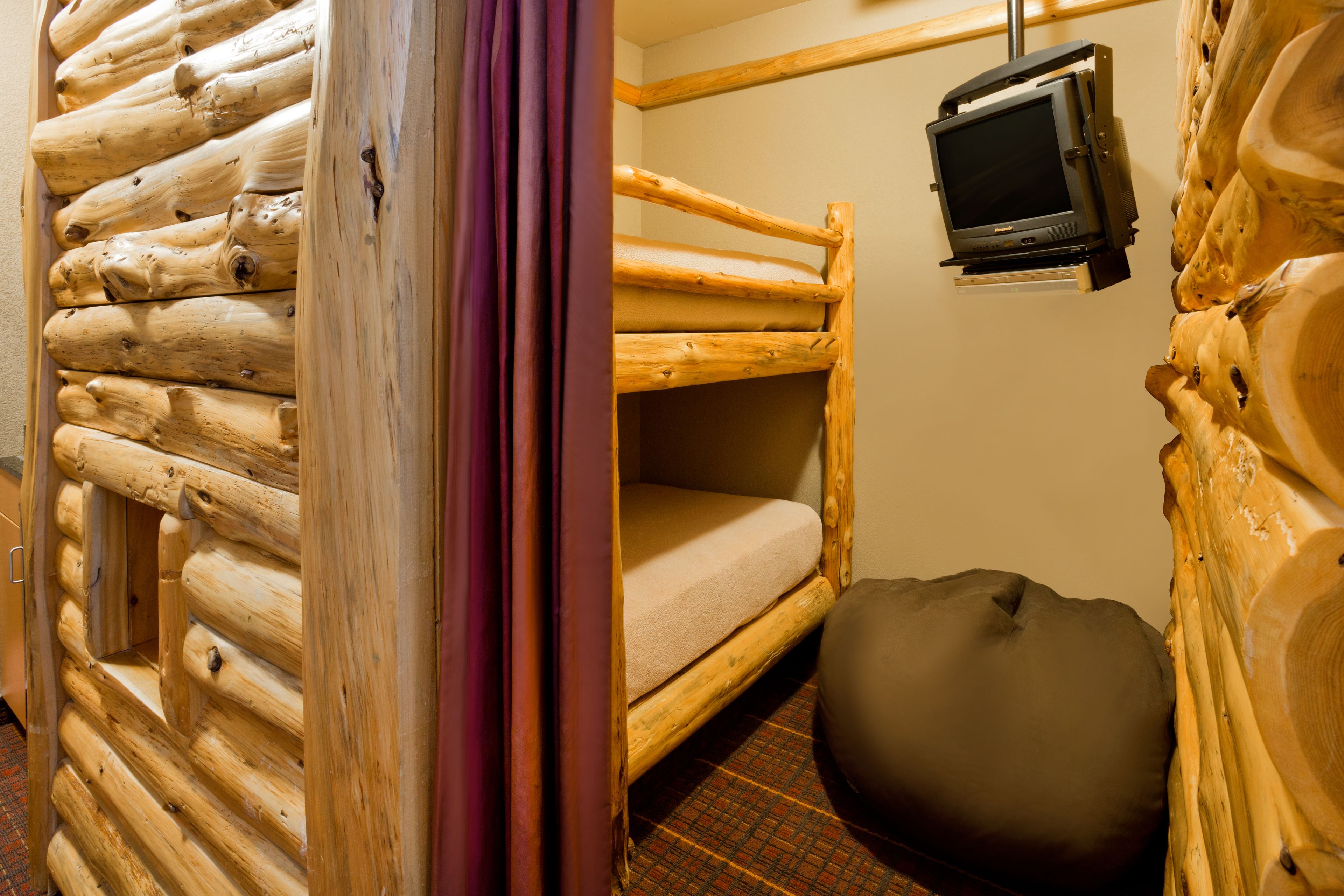 Ein Blockhauszimmer mit Etagenbett, einem an der Wand befestigten Fernseher und einem runden Sitzsack.