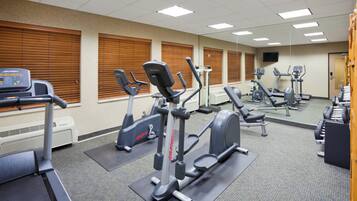 Un gimnasio con varias máquinas de ejercicio, un televisor y un espejo.