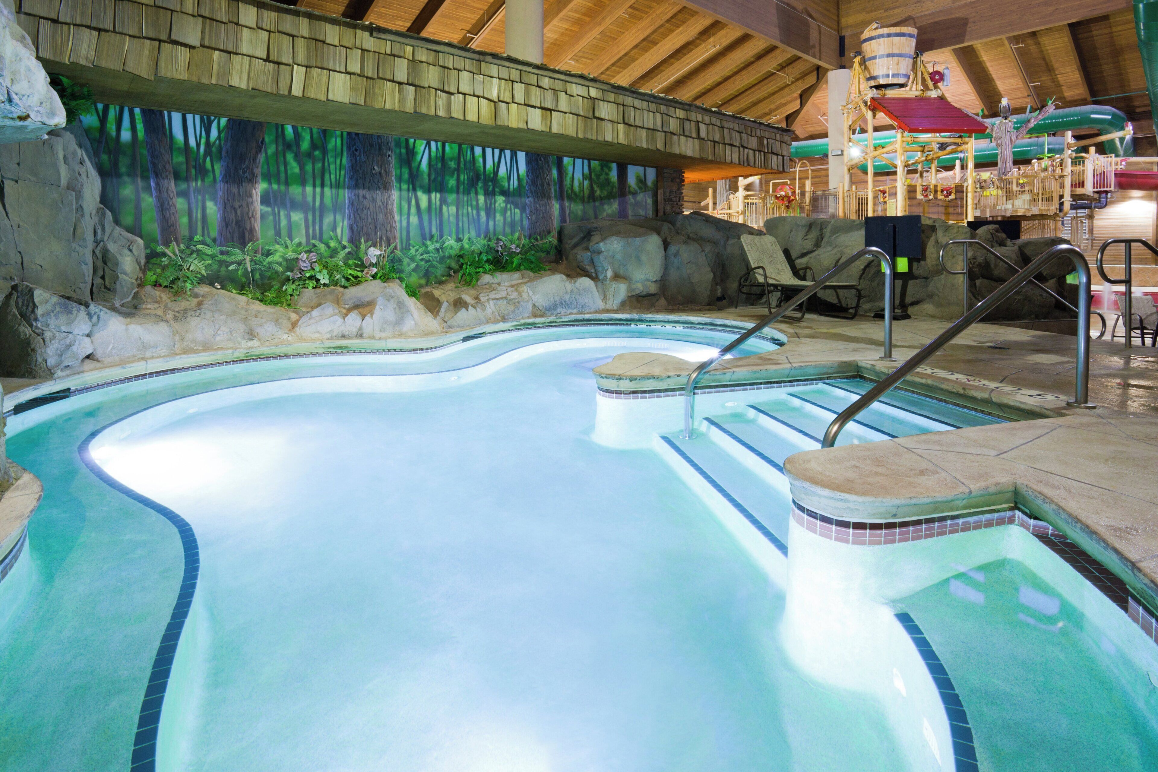 An indoor swimming pool with a wooden ceiling and a mural of a forest.