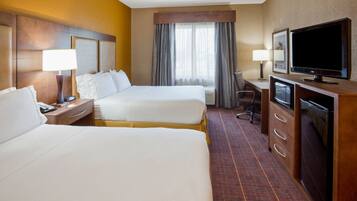 A hotel room with two beds, a desk, a television, and a window with curtains.