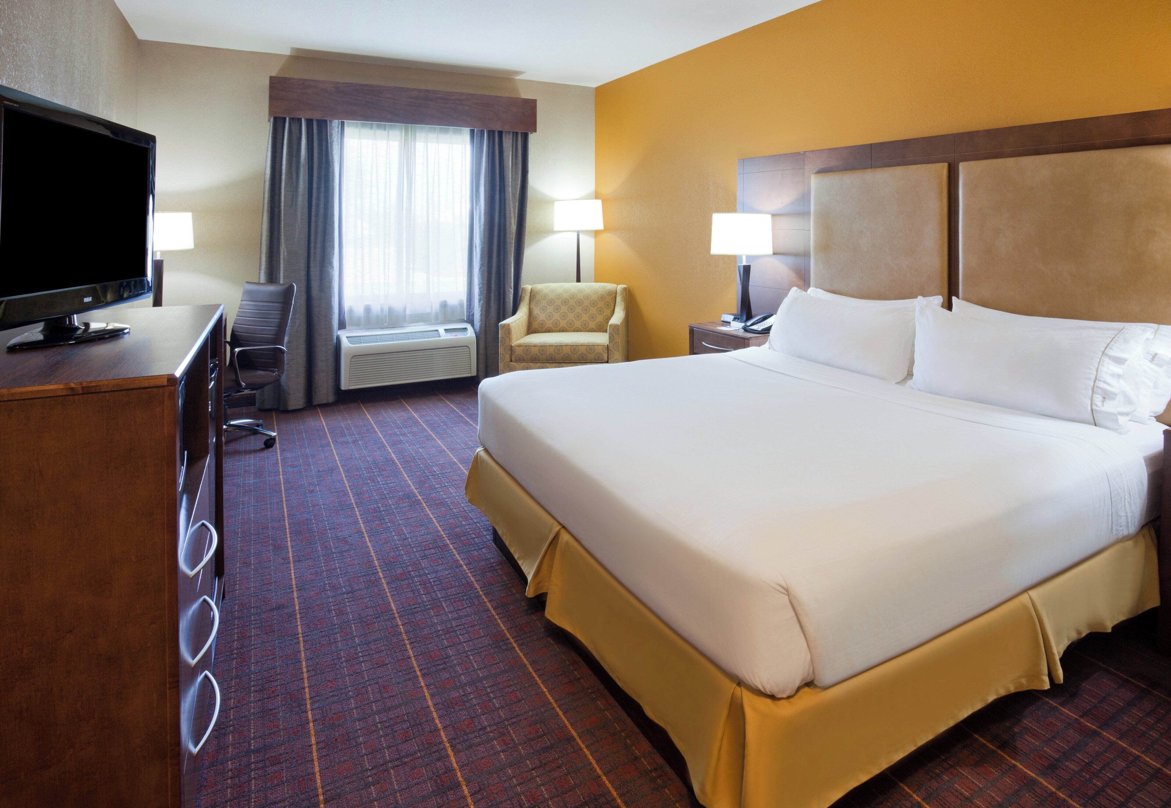 A hotel room with a large bed, a desk with a television, a chair, and a window with curtains.