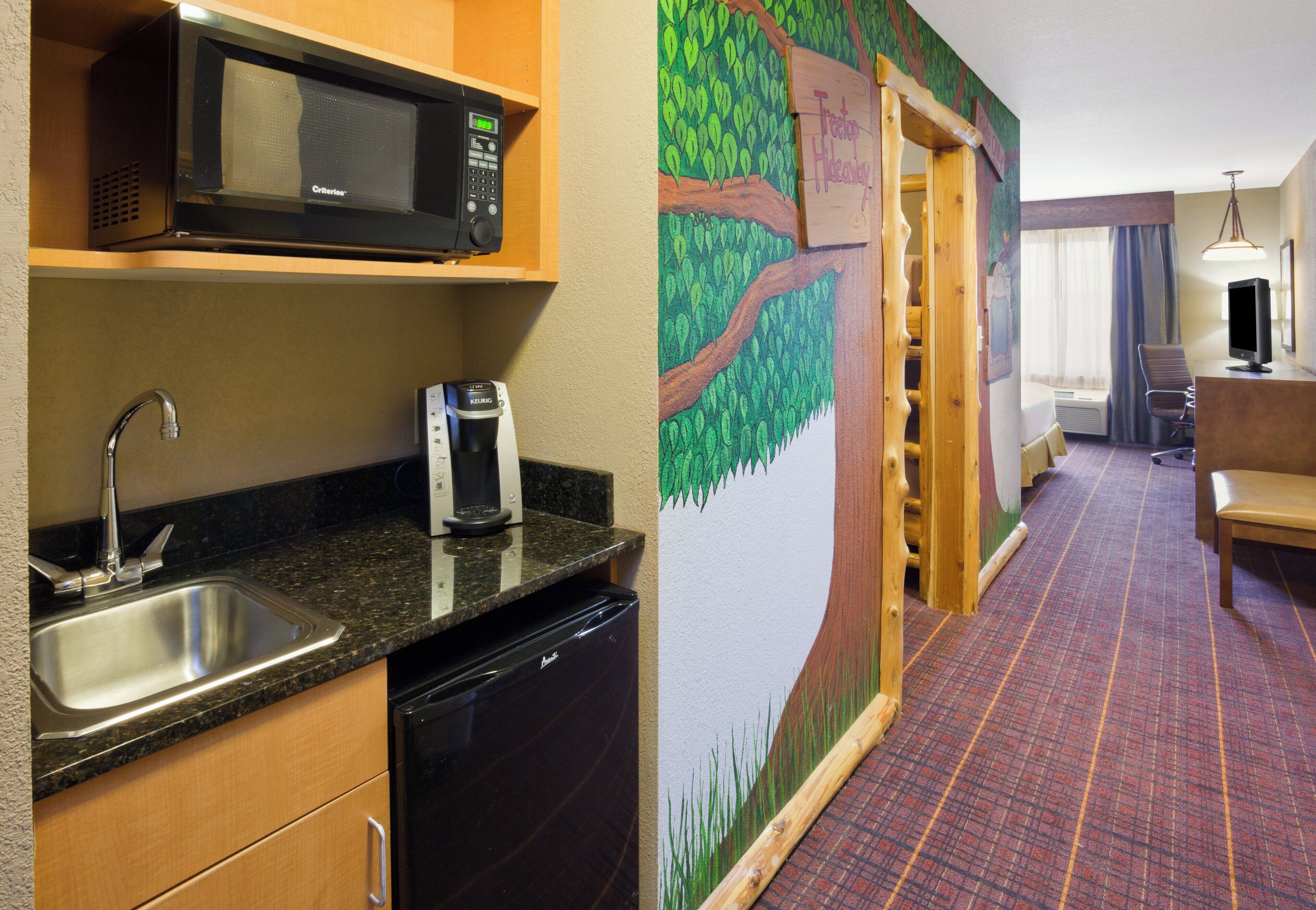 A hotel room with a kitchenette, including a microwave, coffee maker, and dishwasher.