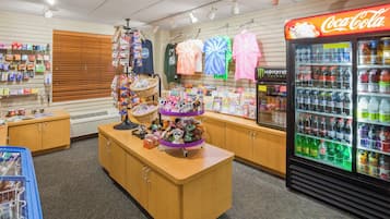 Una tienda minorista con un refrigerador Coca-Cola, estantes llenos de diversos productos y una exhibición de peluches.