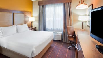 Habitación de hotel con una cama grande, un escritorio con televisor de pantalla plana, una silla, una lámpara y un equipo de aire acondicionado.