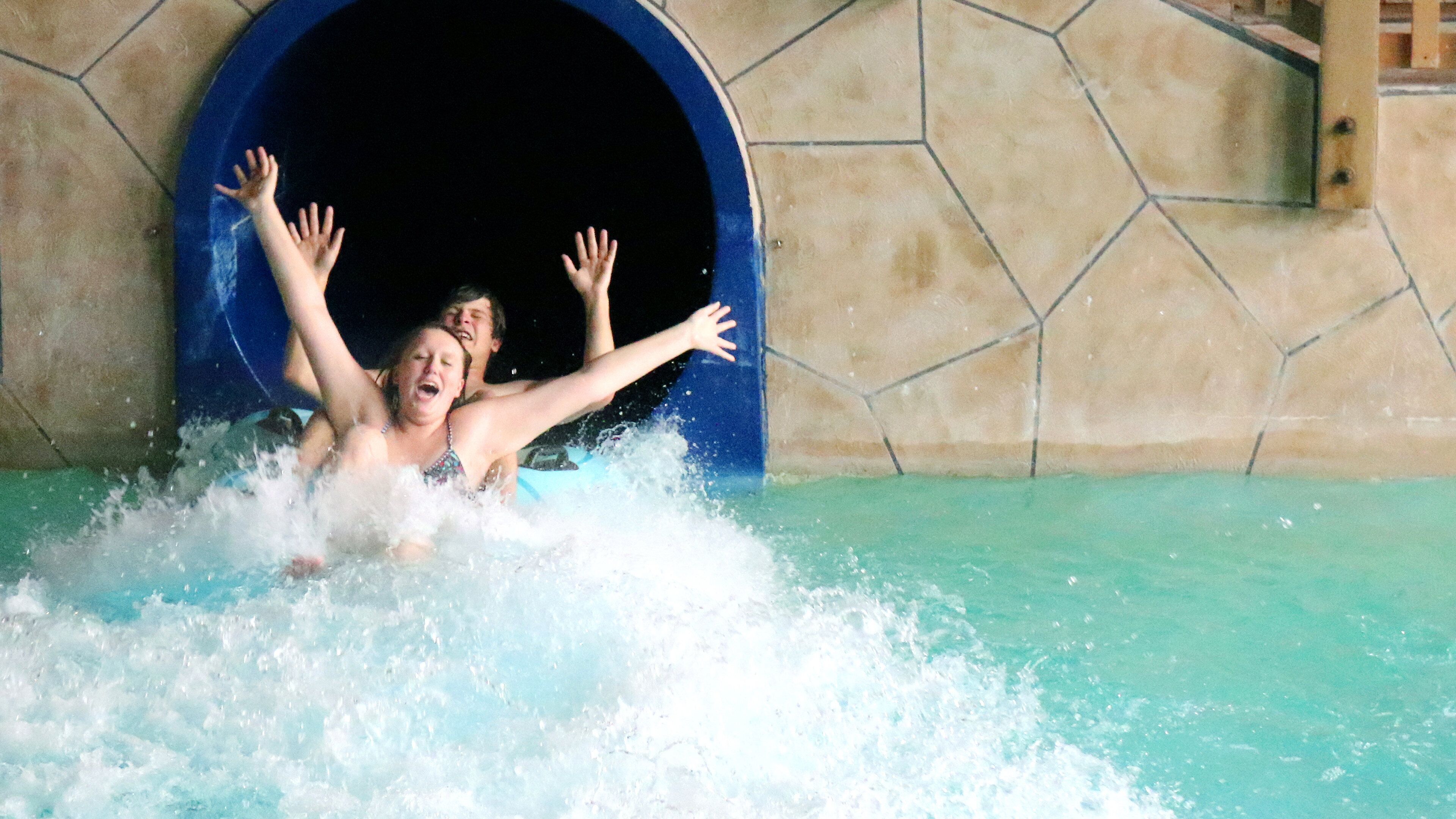 A person in a swimming pool with arms raised, water splashing around.