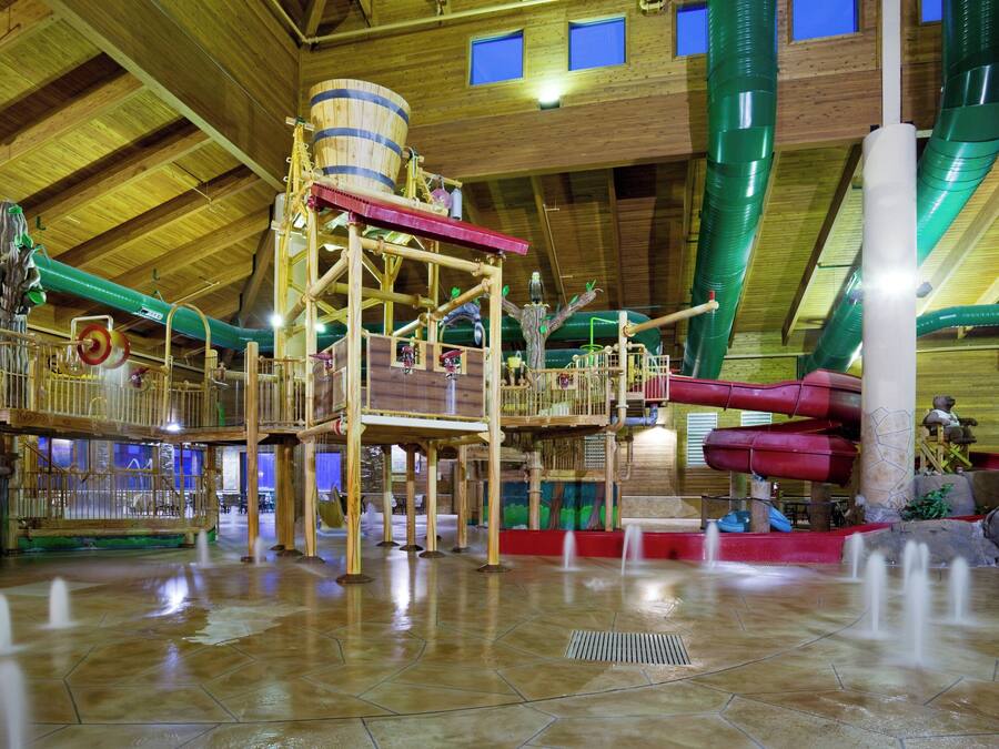 Parque acuático interior con estructuras de madera, toboganes y un techo alto.