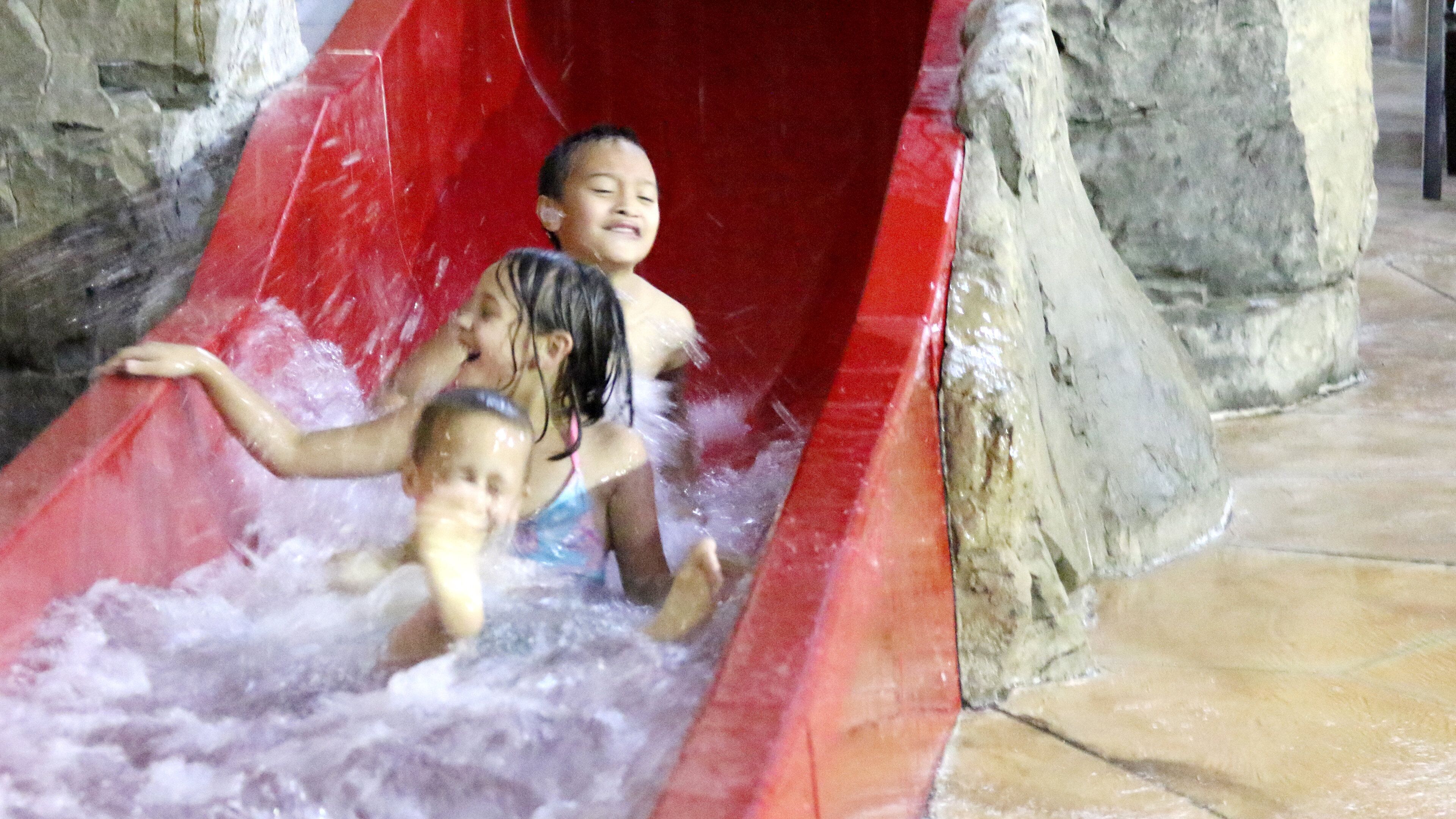 Children sliding down a red water slide with water splashing around them.