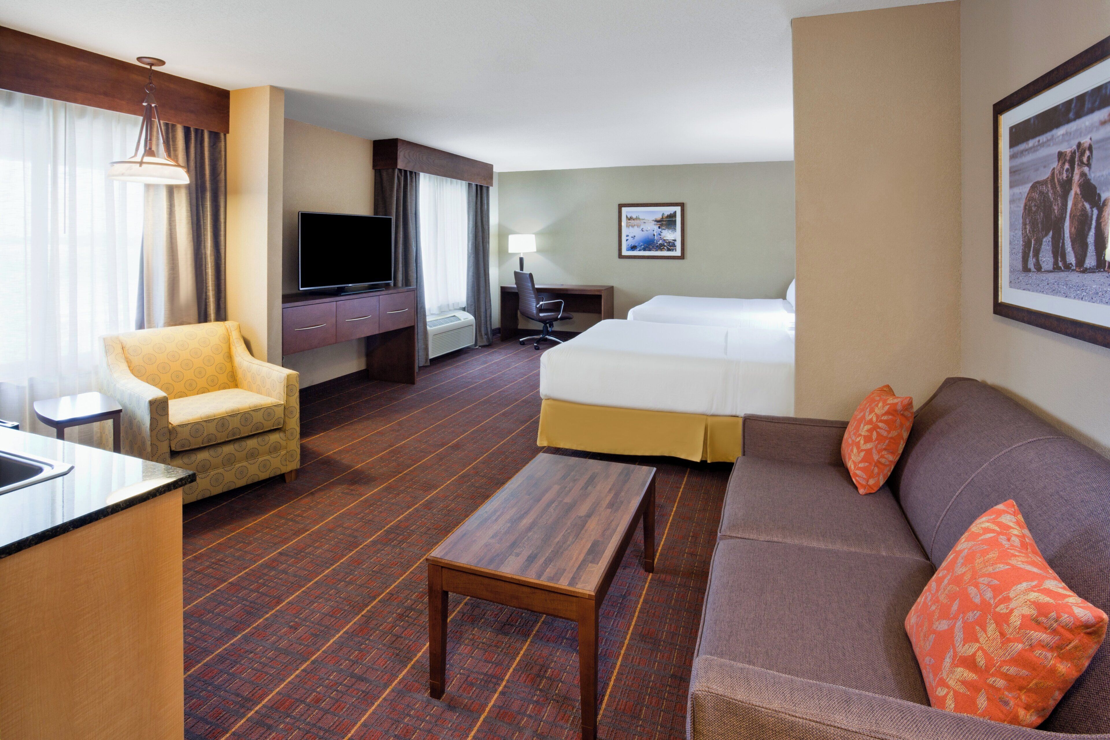 Habitación de hotel con cama, sofá, sillón, escritorio, televisor y un cuadro en la pared.