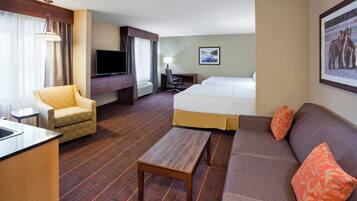 Habitación de hotel con cama, sofá, sillón, escritorio, televisor y un cuadro en la pared.