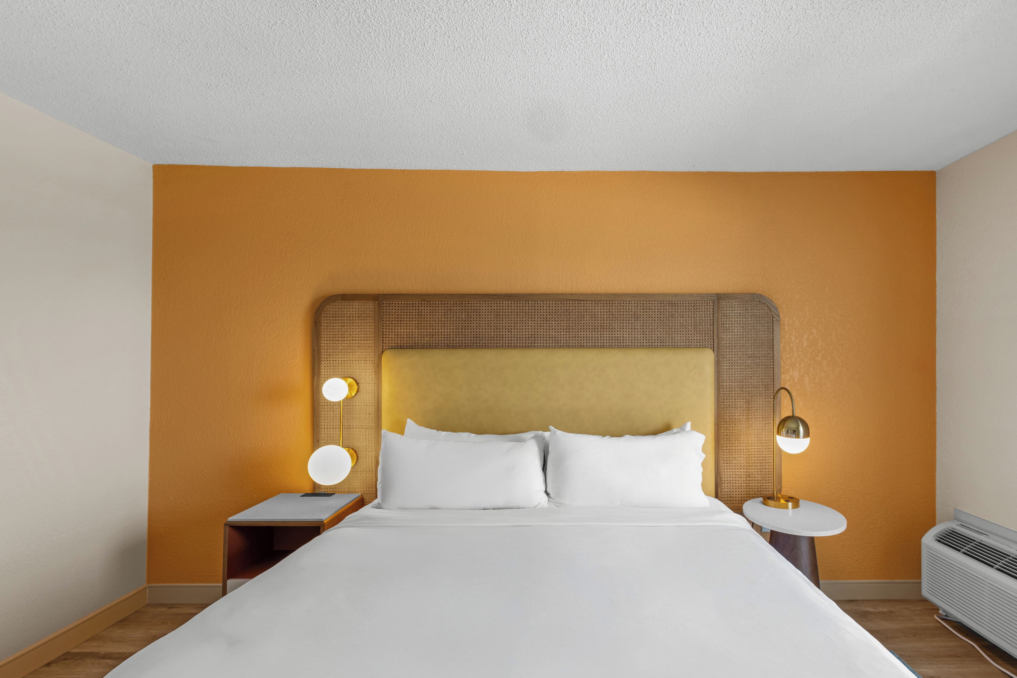 A hotel room with a large bed, two bedside tables, and a wall-mounted air conditioner.