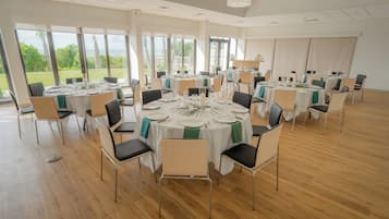 Un vaste espace dédié à la salle à manger, avec des tables rondes, des chaises et de grandes fenêtres donnant sur l’extérieur.