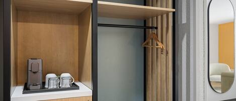 Ein modernes Hotelzimmer mit einem Holzschrank, einer Kaffeemaschine und einem Kleiderhaken.