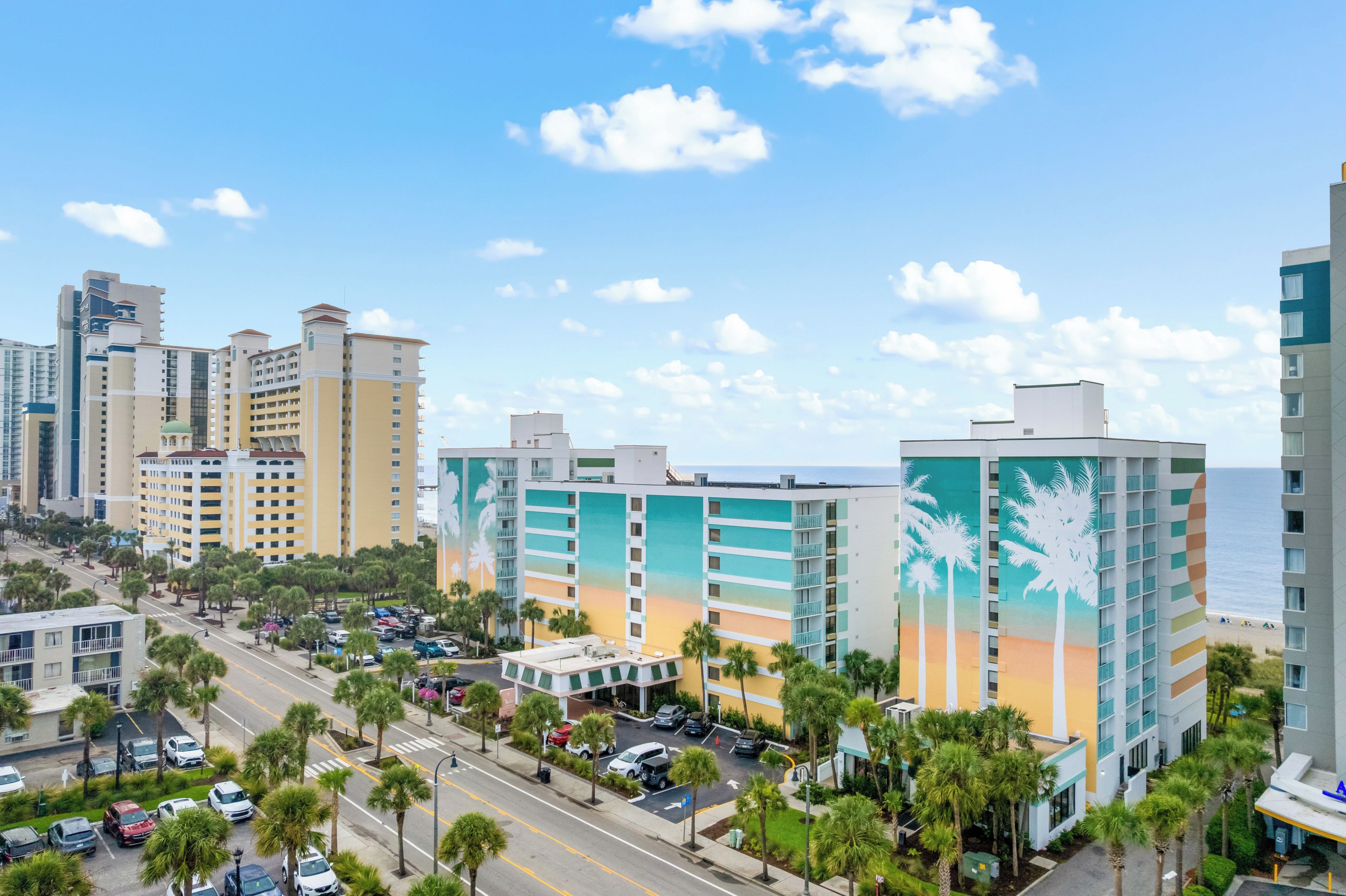 A multi-story hotel with a parking lot and a view of the ocean.