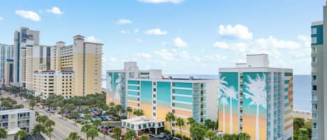 A multi-story hotel with a parking lot and a view of the ocean.