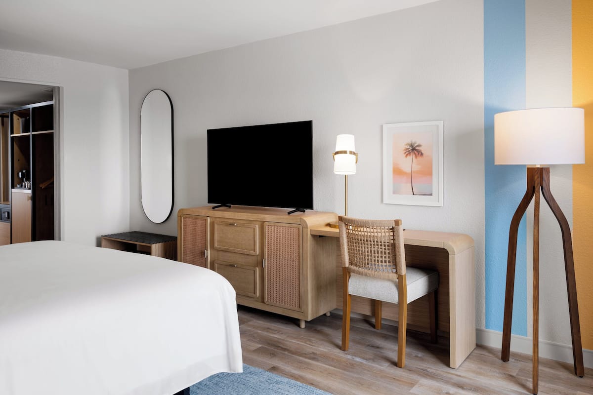 A hotel room with a bed, a desk, a television, a chair, and a lamp.