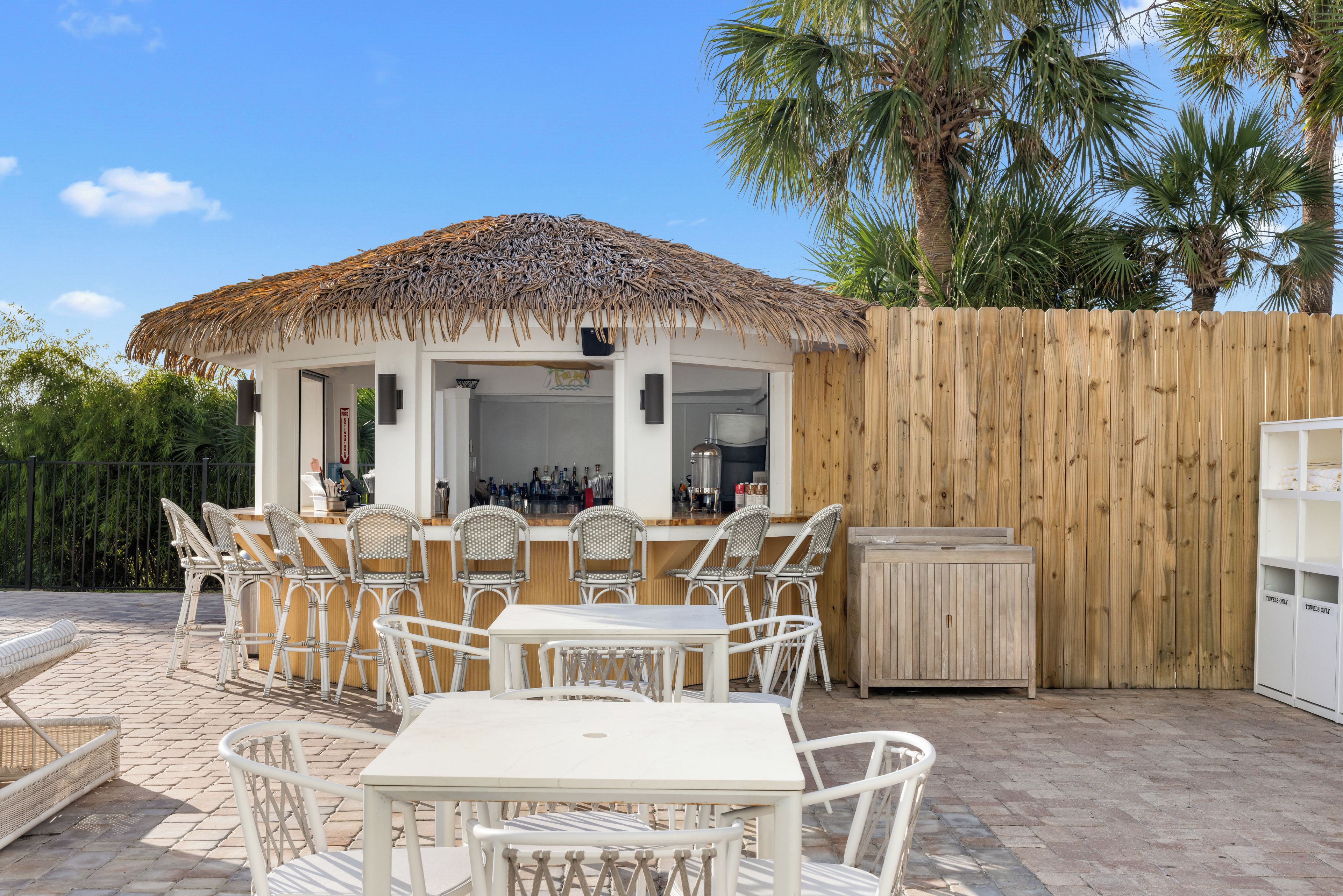 An outdoor patio with a thatched roof, white wicker furniture, and a bar area.