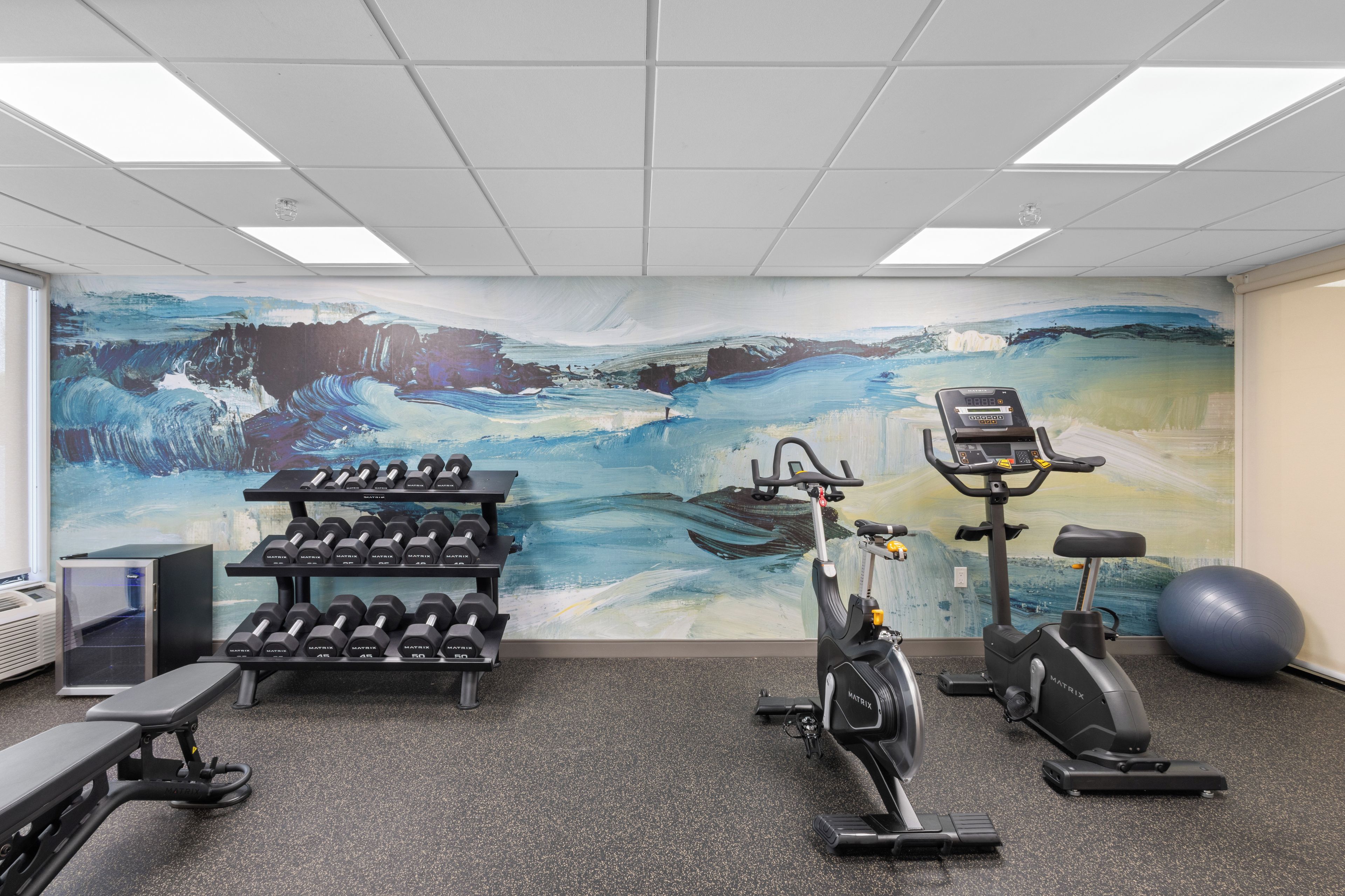 Un gimnasio con equipamiento de ejercicio, un mural en la pared y una cinta de correr.