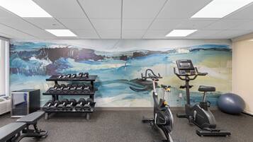 Un gimnasio con equipamiento de ejercicio, un mural en la pared y una cinta de correr.
