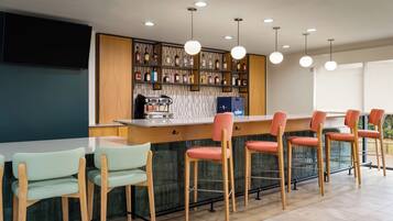 Un espace bar avec des tabourets en bois, un comptoir avec une machine à café et des étagères remplies de bouteilles.