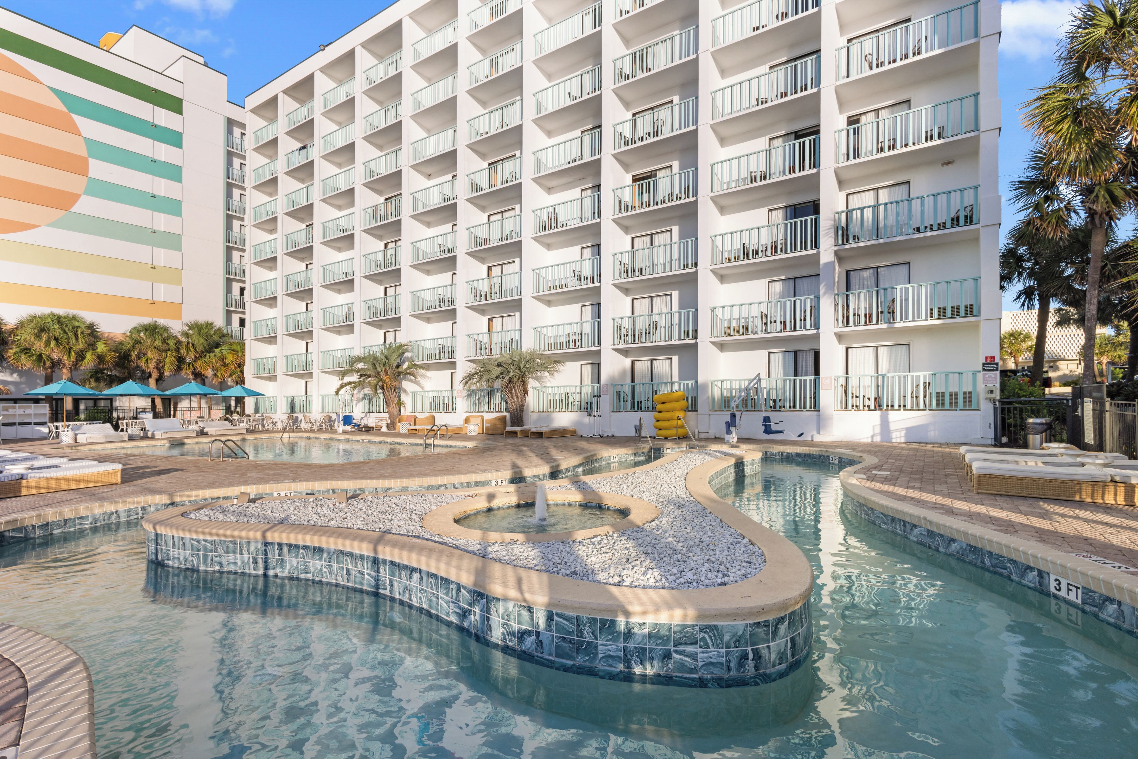 Ein Hotel mit mehreren Balkonen, einem Pool mit Springbrunnen und Außenmöbeln.