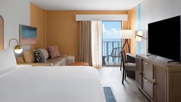 Une chambre d’hôtel avec un grand lit, un bureau avec une télévision, une chaise, un canapé avec des coussins, une petite table et une fenêtre avec des rideaux.