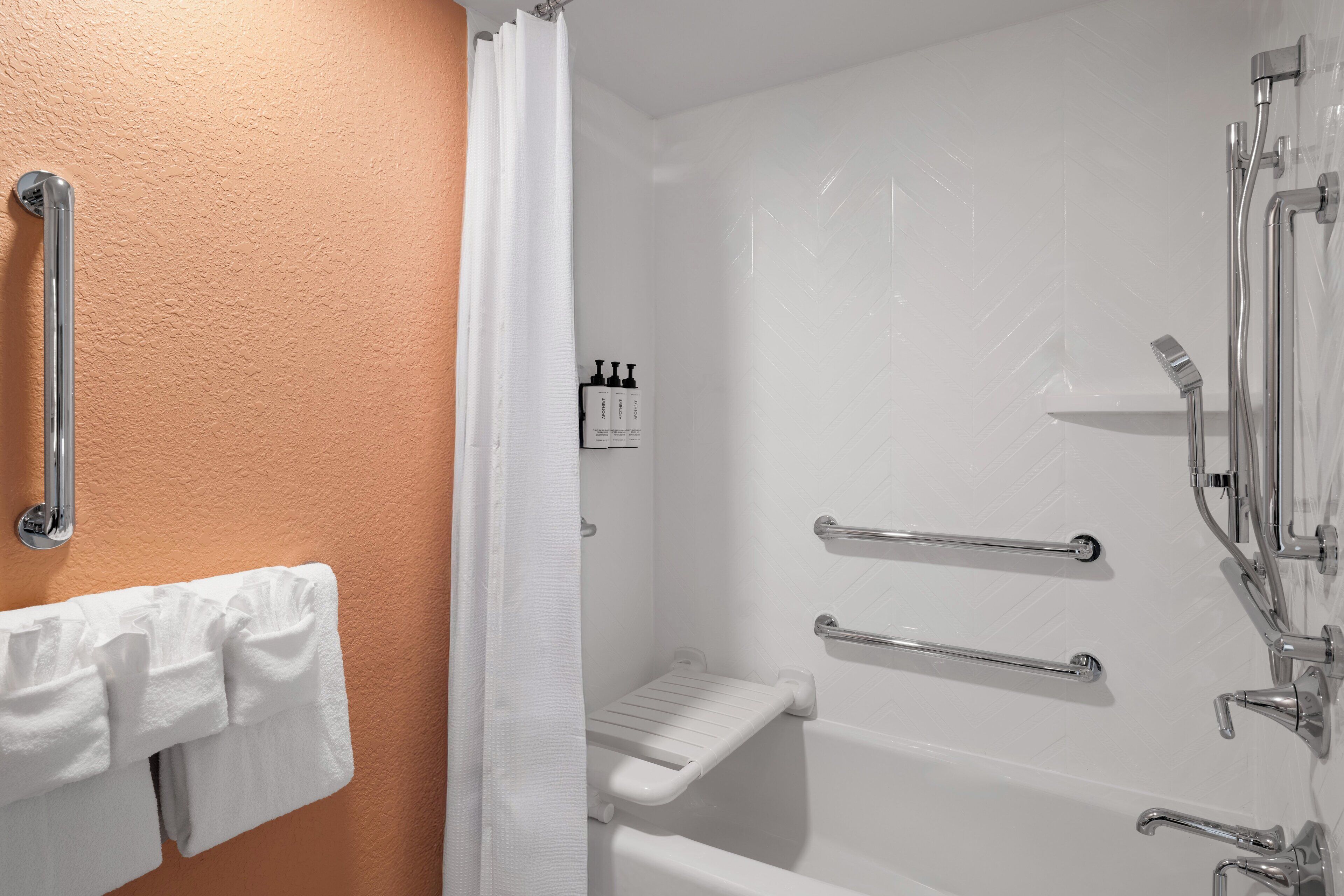 Une salle de bain équipée d’une douche, de barres d’appui, d’une baignoire blanche et d’un porte-serviettes.
