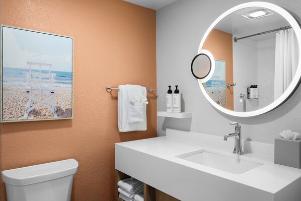 A bathroom with a white sink, a round mirror, a towel rack with a white towel, and a framed picture of a beach scene.