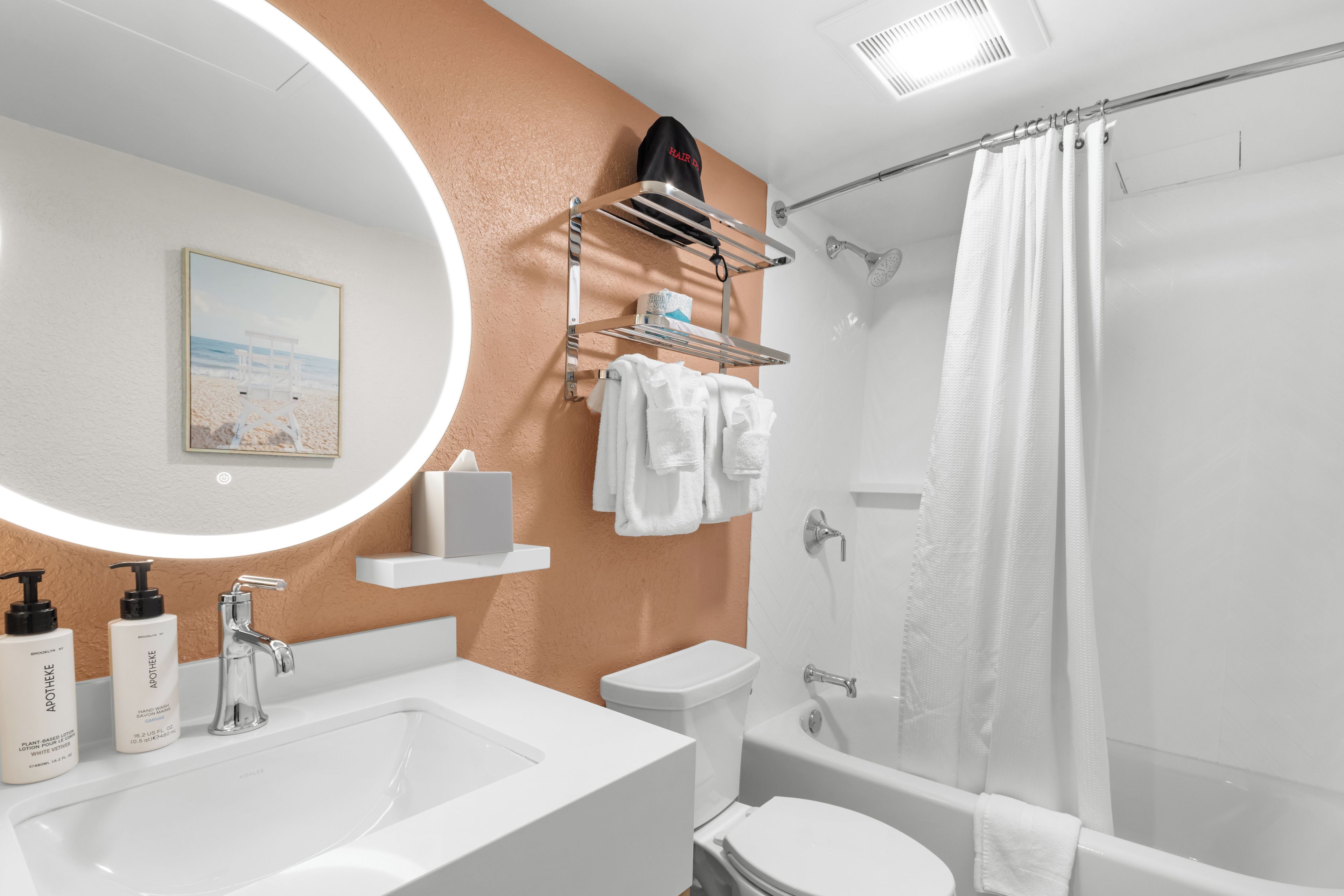 A modern bathroom with a large oval mirror, a sink, a toilet, and a shower area.