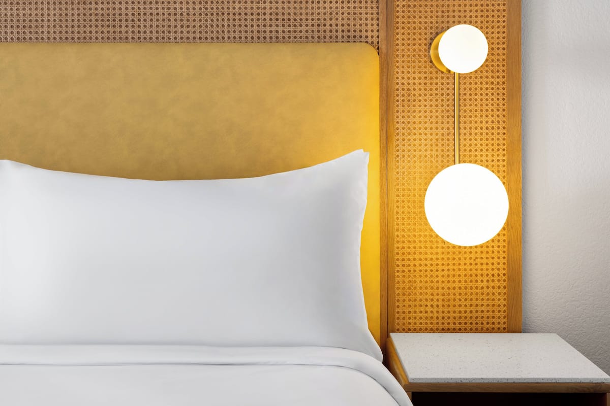 A bed with white bedding, a wooden headboard, and two wall-mounted circular lights.