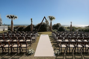 An outdoor wedding venue with a white aisle carpet, wooden chairs, and palm trees. - voco The Shelby - Myrtle Beach by IHG (Myrtle Beach)
