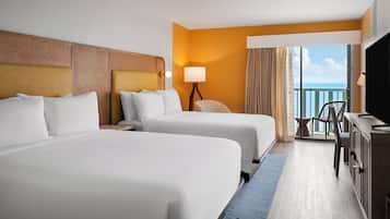 A hotel room with two beds, a desk, a chair, and a balcony with a view.