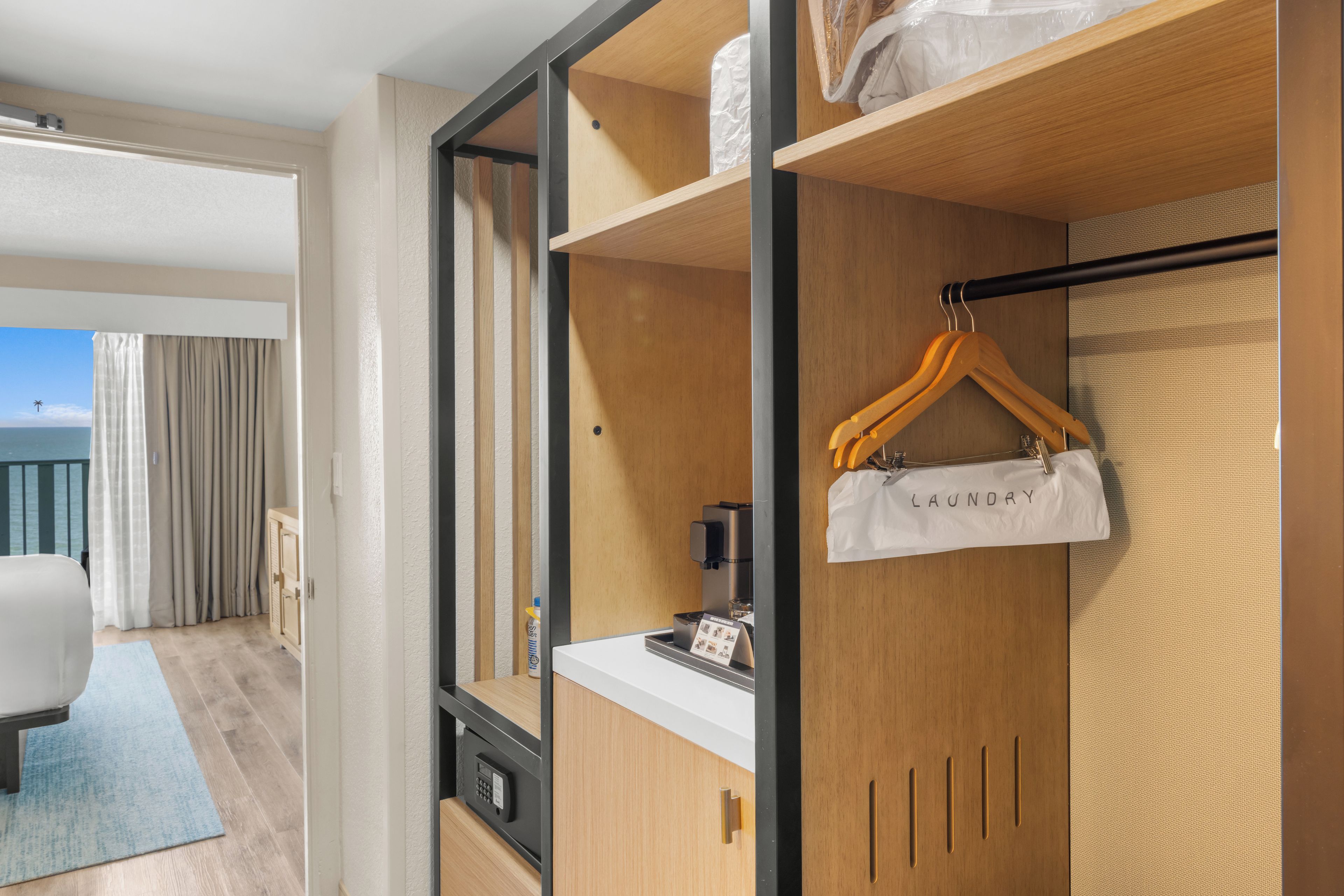 A hotel room with a wardrobe, a small table with a coffee machine, and a view of the sea.