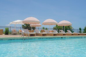 Una piscina con sillas de descanso y sombrillas, rodeada por una valla y palmeras.