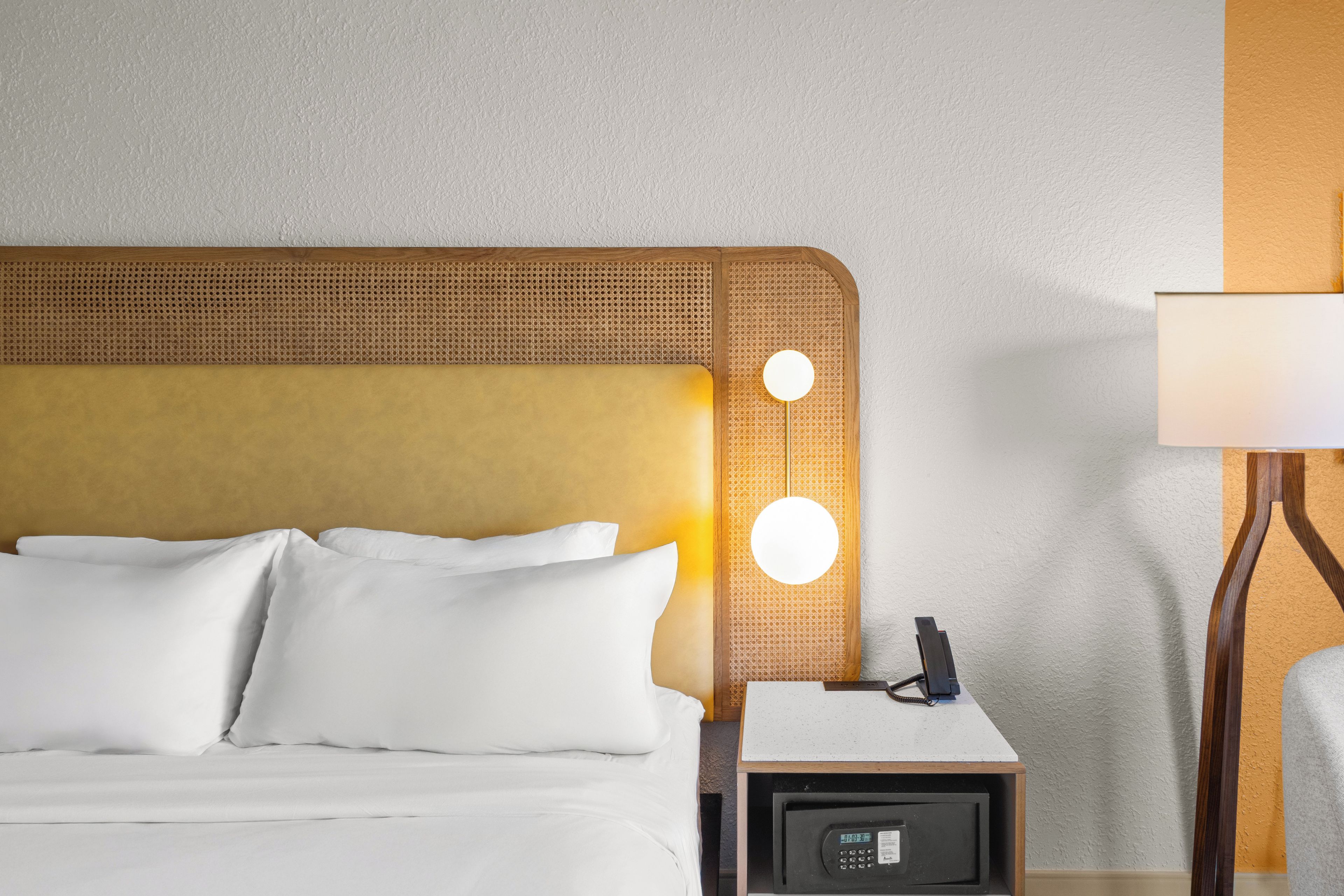 A hotel room with a bed, a nightstand, a lamp, and a wall-mounted light fixture.