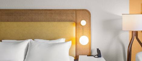 A hotel room with a bed, a nightstand, a lamp, and a wall-mounted light fixture.