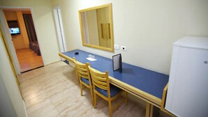Una habitación pequeña con una mesa azul, dos sillas de madera, un refrigerador blanco y un espejo en la pared.