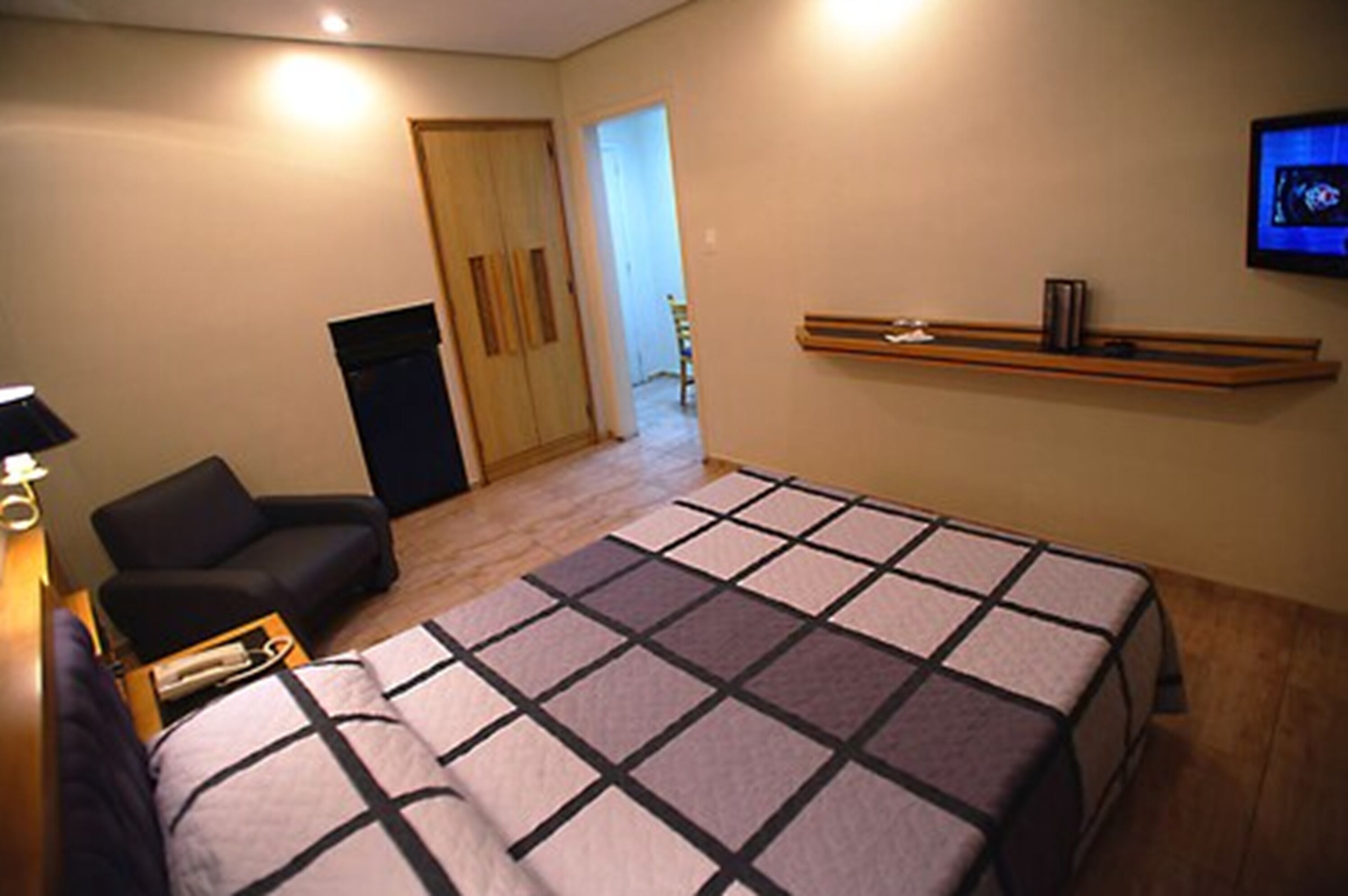 A bedroom with a bed, a chair, a TV, and a wooden shelf.